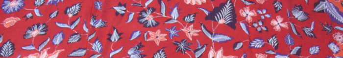 A red batik fabric with navy and purple colours and orange flowers.