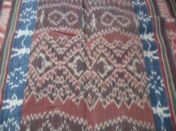 A cotton blanket in red, blue, green, brown, and white, covered in various motifs including some patterns and human figures.